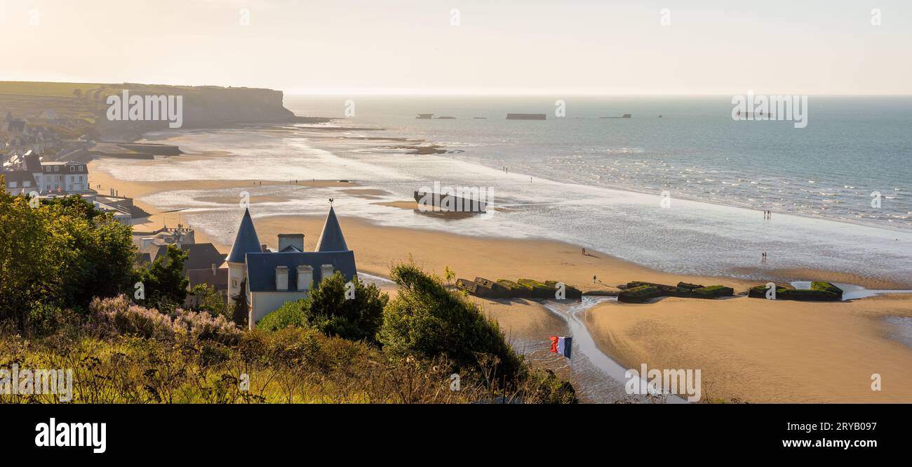 Blick auf den Strand von Arromanches in der Normandie bei Sonnenuntergang mit Überresten des Mulberry Hafens aus dem Zweiten Weltkrieg auf dem Sand und den Phoenix Caissons im Meer. Stockfoto