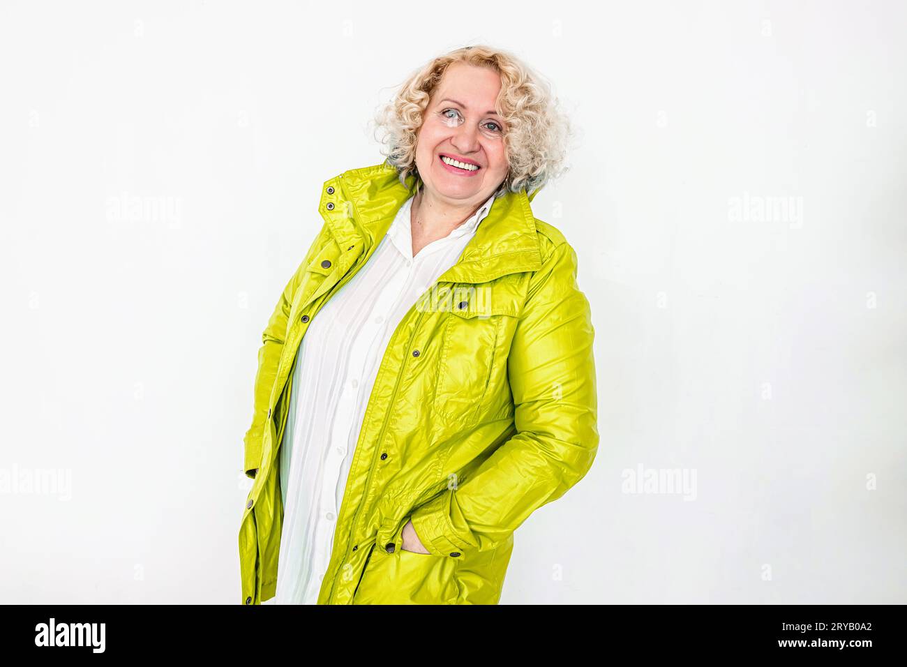 Ältere Frau in gelber Jacke lächelnd auf weißem Wandhintergrund Stockfoto