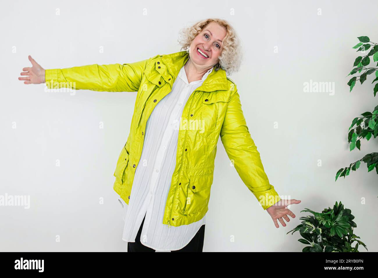 Glückliche Frau in gelber Jacke, die mit den Armen an den Seiten steht Stockfoto