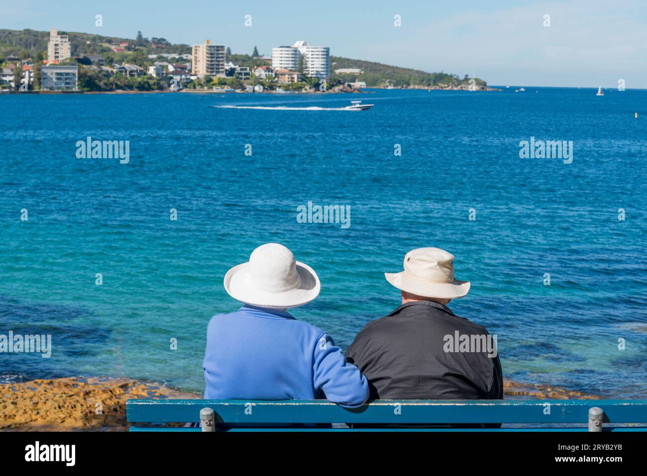 Ein älteres Paar, das an einem sonnigen Wintermorgen in Australien vom Delwood Harbour Beach aus über den Hafen von Sydney nach Smedley's Point Manly blickt Stockfoto