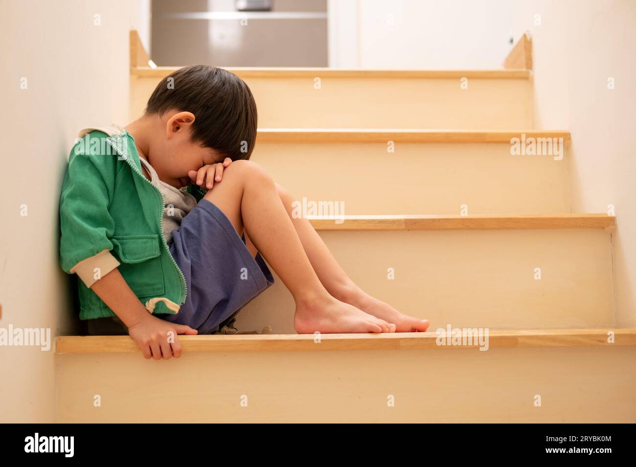 Ein trauriger asiatischer Junge sitzt mit dem Kopf auf den Stufen. Traurig Stockfoto