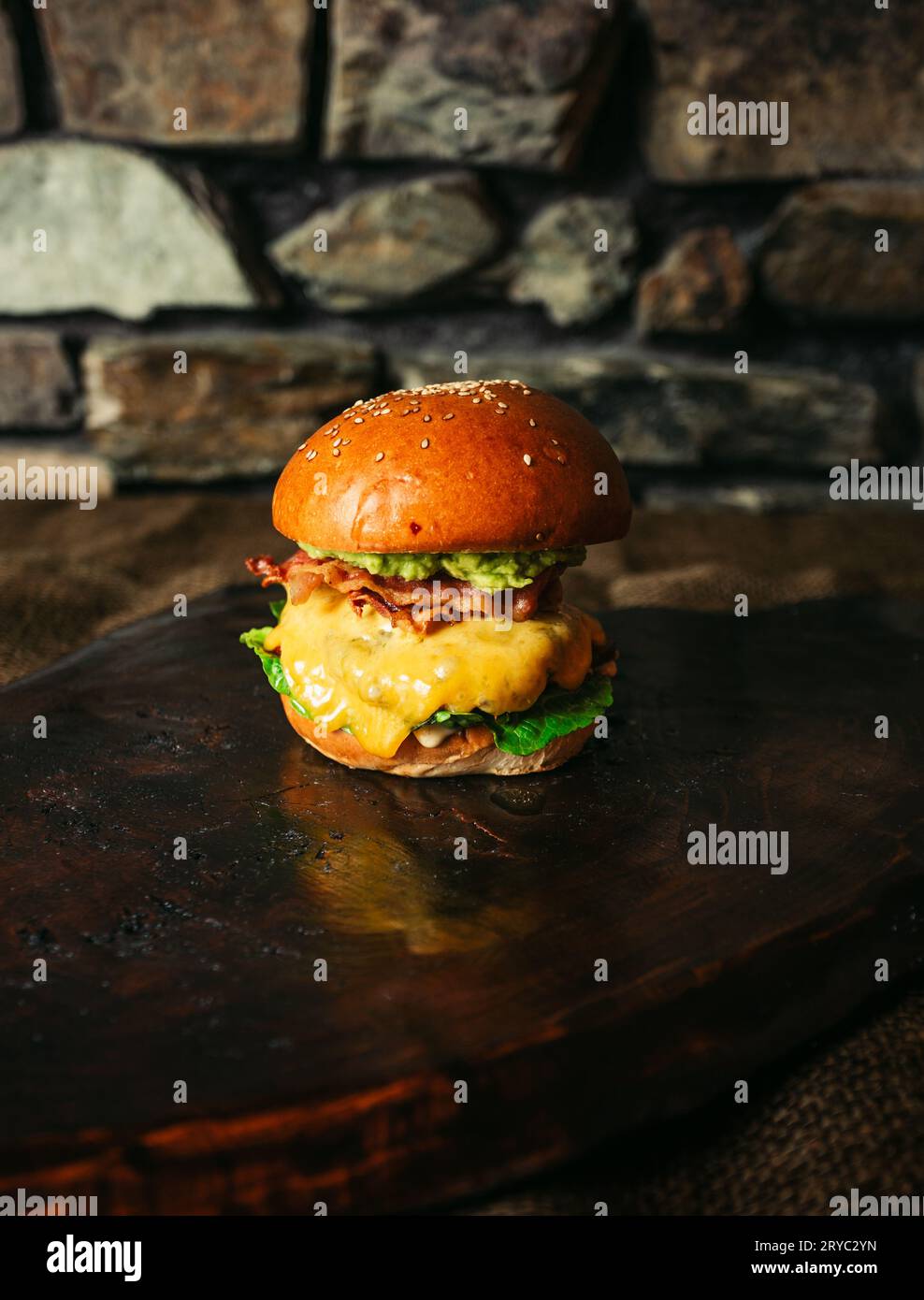 Beleuchtetes Foto von amerikanischem Hamburger mit Chuck-Roll-Fleisch, Cheddar-Käse und anderen Zutaten auf dunklem Hintergrund. Stockfoto