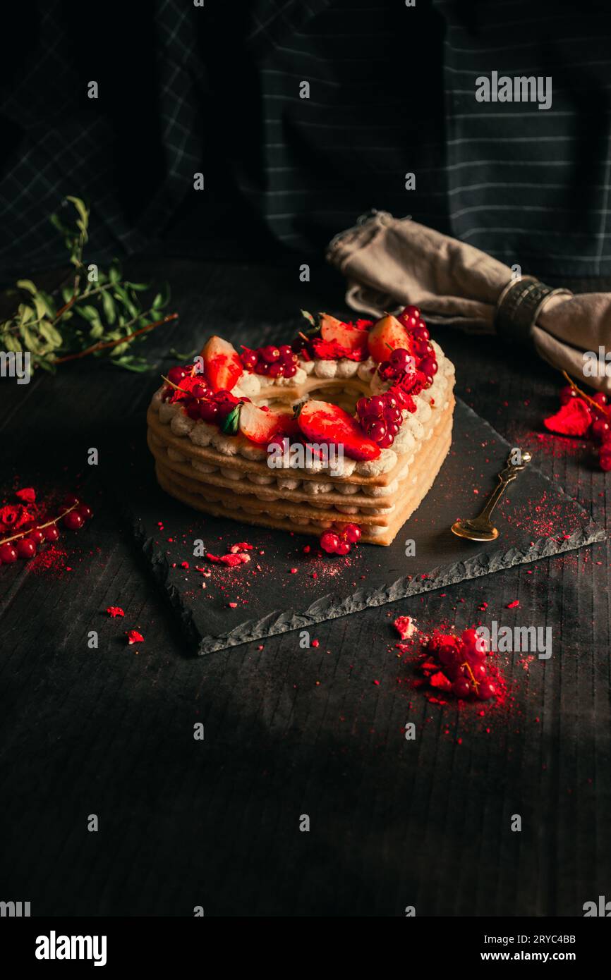 Süßwarenkonzept - rot-weißer Kuchen in Herzform für St. Valentinstag auf schwarzem Tisch (Teller). Süßes und romantisches Geschenk - Erdbeerkuchen Stockfoto