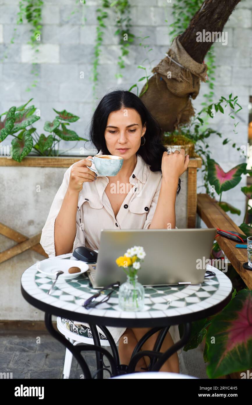 Junge ukrainische brünette Frau, die mit Laptop arbeitet und Kaffee im Café trinkt Stockfoto