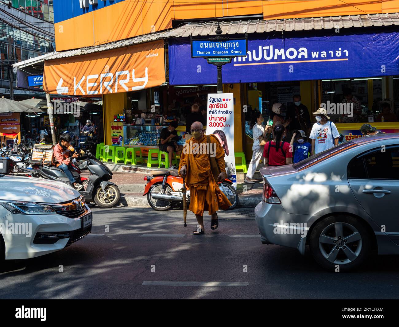 Ein buddhistischer Mönch, gekleidet in einem traditionellen orangen Safranmantel und mit einer Gesichtsmaske, überquert eine Bangkok, Thailand Straße. Stockfoto