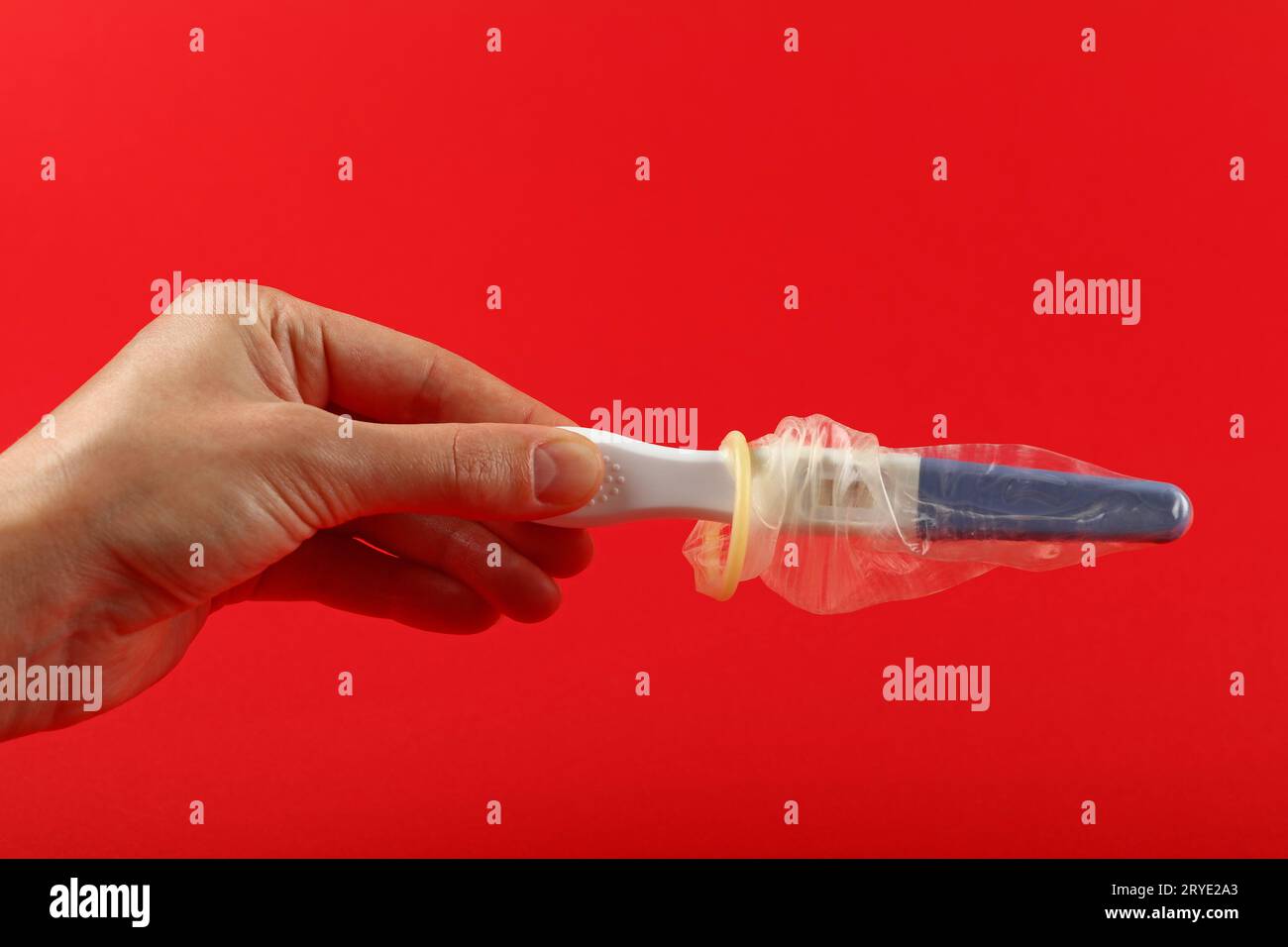 Frauenhand hält Schwangerschaftstest mit Kondom Stockfoto