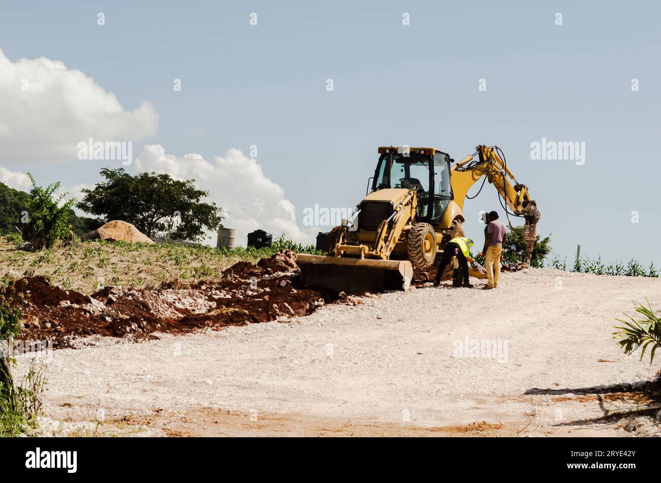 An einem Frontlader mit Rädern, die vom Boden angehoben werden, arbeiten Männer am Straßenprojekt. Stockfoto