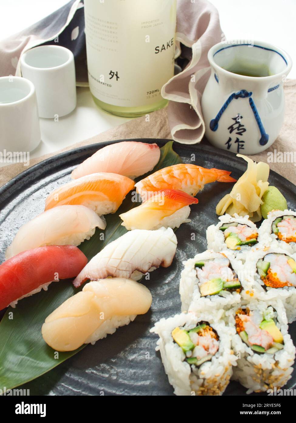 Farbenfrohe Auswahl an Nigiri-Sushi auf Teller mit kalifornischen Brötchen, serviert mit Sake, im japanischen Restaurant. Stockfoto