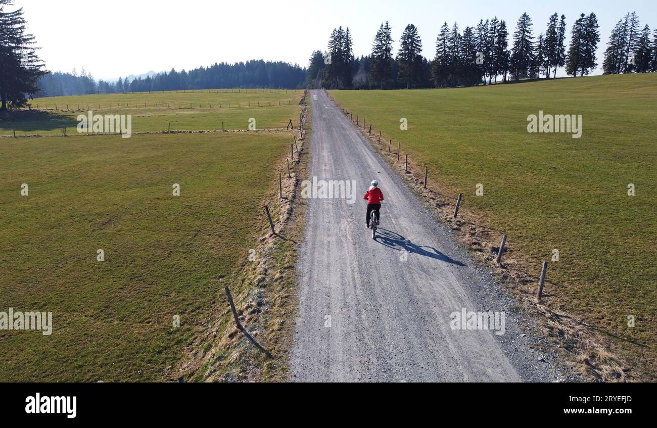 Drohnenaufnahme einer Radfahrerin auf einsamer Straße mit Schatten Stockfoto