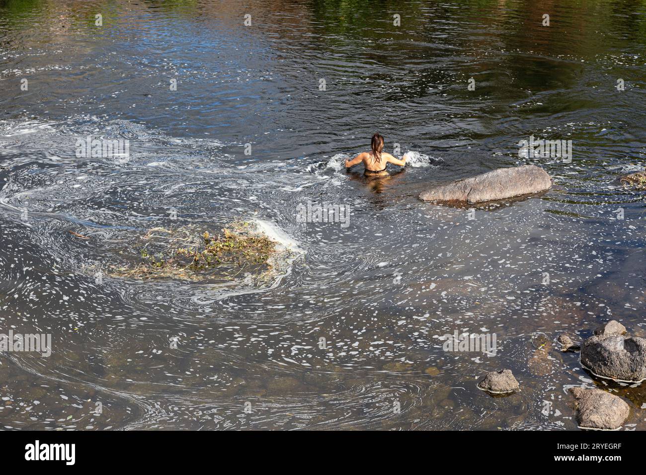 Nicht erkennbare Frau schwimmt in einem verschmutzten Fluss durch Reinigungsmittel oder Seife Stockfoto