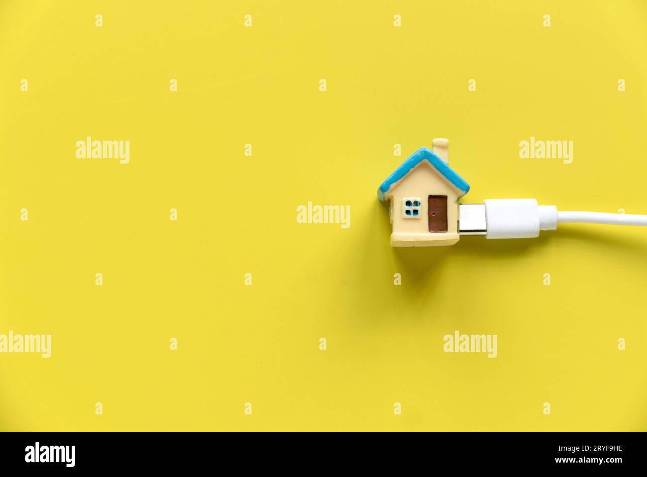 Haus- und Versorgungskonzept. Miniatur-Gehäuse an einem weißen Kabel über einem gelben Backgorund befestigt Stockfoto