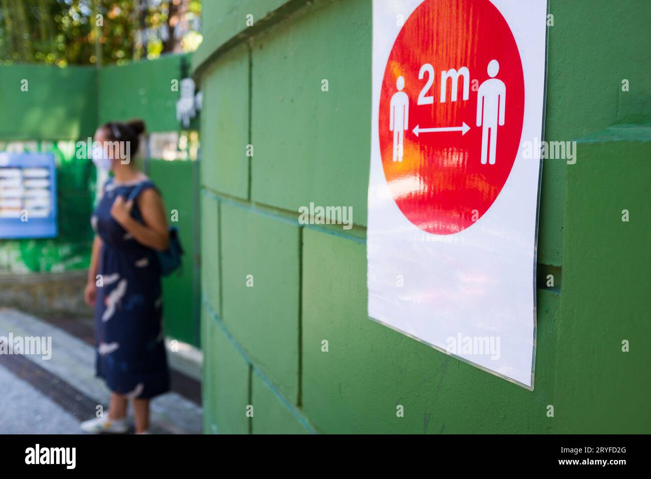 Rotes 2m-Zeichen für soziale Distanz an der grünen Wand auf der Straße mit Frau im Hintergrund Stockfoto