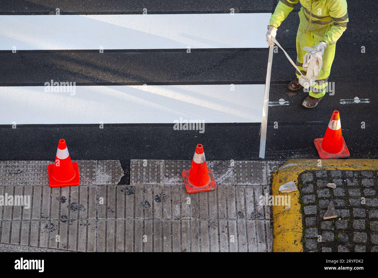 Arbeiter, der Klebeband entfernt hat, nachdem er einen Zebrastreifen auf einer Stadtstraße gemalt hat Stockfoto