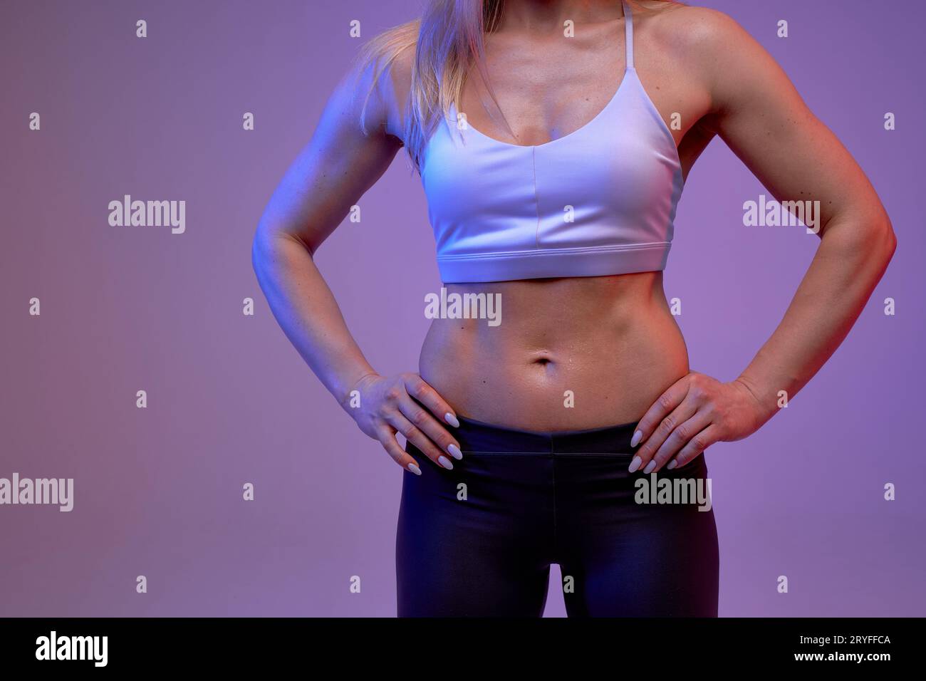 Starke, muskulöse, sportliche Frau mit sechserpack-bauchmuskeln, Mädchen mit den Händen auf den Hüften, die vor der Kamera posiert. Isolierter violetter Hintergrund. Zugeschnittenes Foto Stockfoto