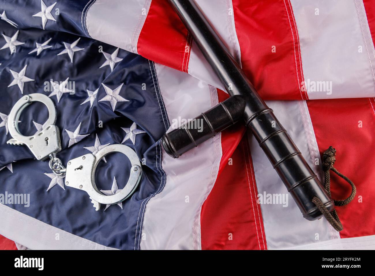 Handschellen aus silbernem Metall und Polizisten-Nachtstock über US-Flagge auf flacher Oberfläche Stockfoto