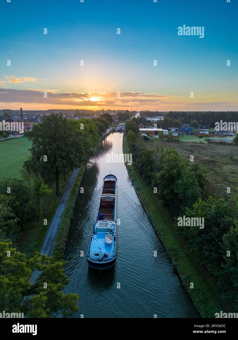 Aus der Vogelperspektive eines farbenfrohen, dramatischen Sonnenaufgangs über einem Kanal mit einem Frachtboot in Belgien. Kanäle mit Wasser für den Transport, Landwirtschaft Stockfoto