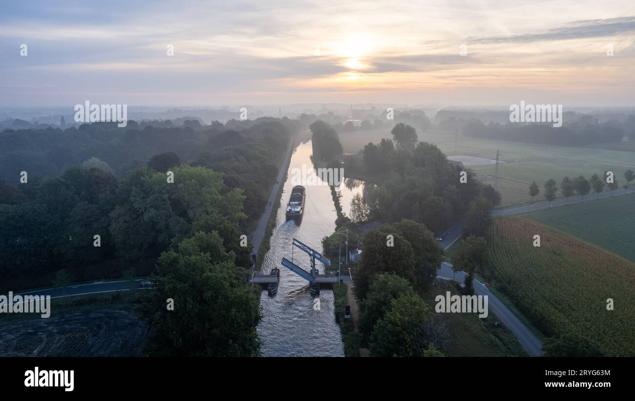 Aus der Vogelperspektive auf einen farbenfrohen, dramatischen Sonnenaufgangshimmel über einem Kanal mit einem Frachtboot, das in Belgien unter einer Zugbrücke vorbeifahren wird. Can Stockfoto