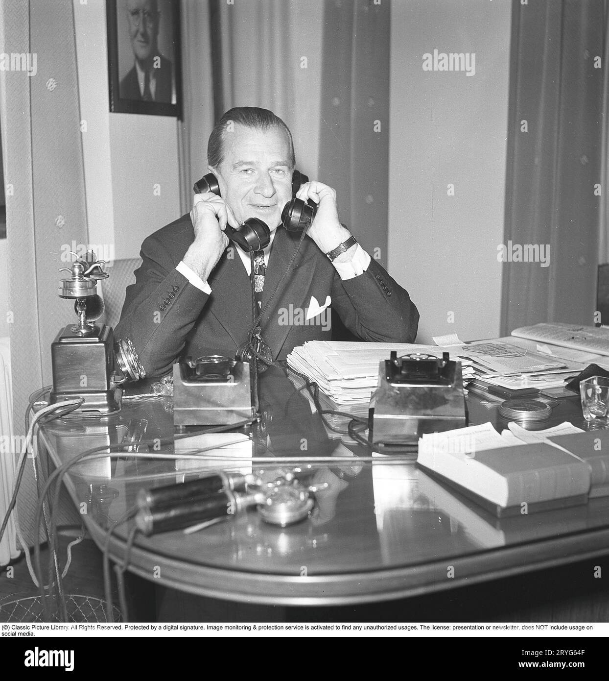 In den 1940er Jahren Ein Mann in einem Büro mit zwei Telefonen, die beschäftigt sind und gleichzeitig in zwei Telefonen sprechen. Schweden 1945. Kristoffersson ref N12-4 Stockfoto