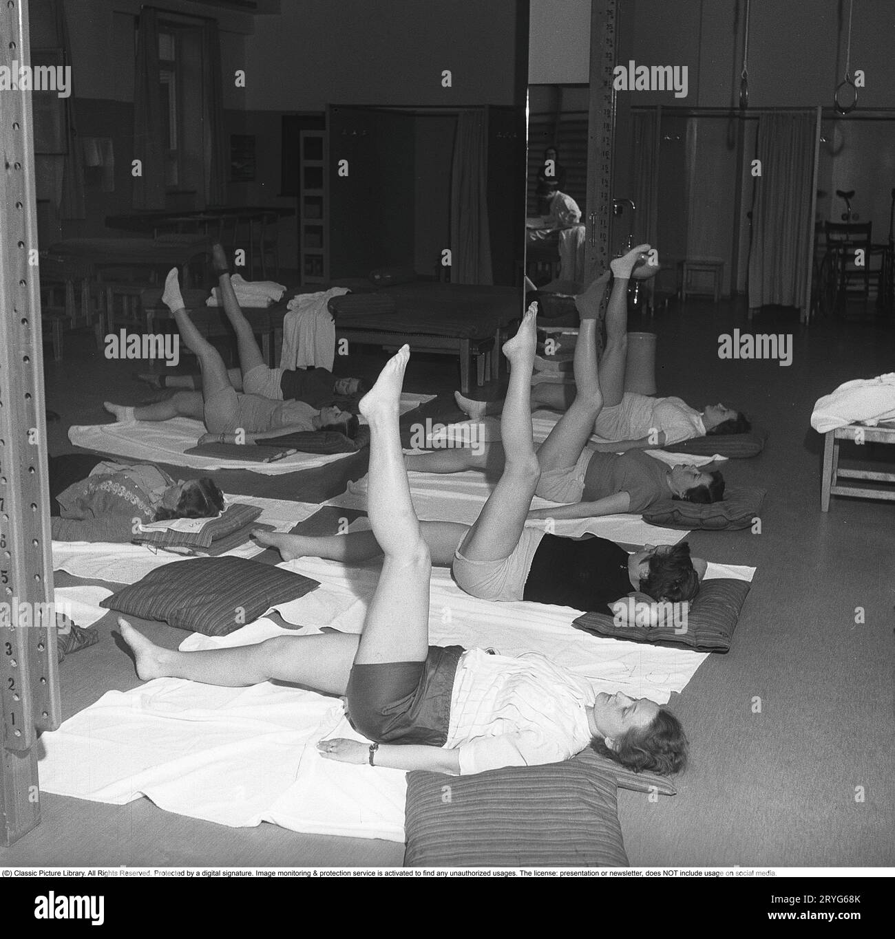 Gymnastik in der Vergangenheit. In einer Turnhalle kniet eine Gruppe von Frauen und streckt ihre Beine in einer Bewegung. Junge Frauen machen eine Pause von der Arbeit und turnen während der Arbeitszeit. Bürogymnastik war eine moderne Erfindung in den 1940er Jahren, als die Gesundheitsfürsorge für Mitarbeiter begann, umgesetzt zu werden. Schweden 1949. Kristoffersson ref AX71-11 Stockfoto