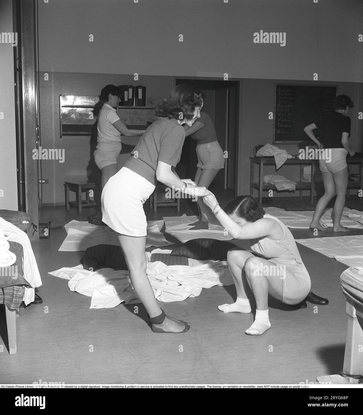 Gymnastik in der Vergangenheit. In einer Turnhalle kniet eine Gruppe von Frauen und dehnt ihre Arme in einer Bewegung. Junge Frauen machen eine Pause von der Arbeit und turnen während der Arbeitszeit. Bürogymnastik war eine moderne Erfindung in den 1940er Jahren, als die Gesundheitsfürsorge für Mitarbeiter begann, umgesetzt zu werden. Schweden 1949. Kristoffersson ref AX72-5 Stockfoto