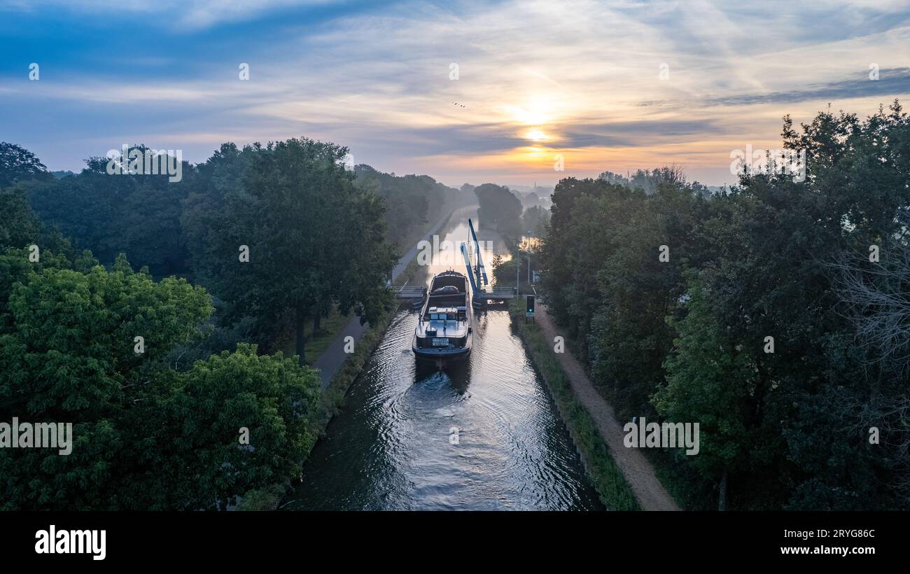 Aus der Vogelperspektive eines farbenfrohen, dramatischen Sonnenaufgangs über einem Kanal mit einem Frachtboot in Belgien. Kanäle mit Wasser für den Transport, Landwirtschaft Stockfoto