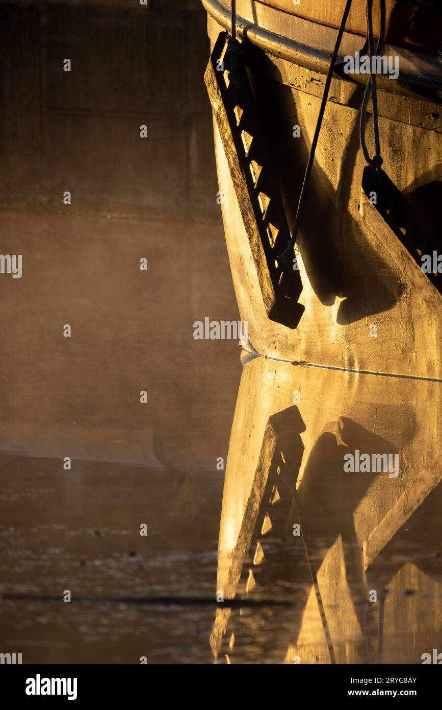 Detail des Bugs eines Bootes im goldenen Licht des Sonnenaufgangs, mit einem Seil, das an den Rumpf eines Bootes gebunden ist, das in einem Hafen vertäut ist Stockfoto