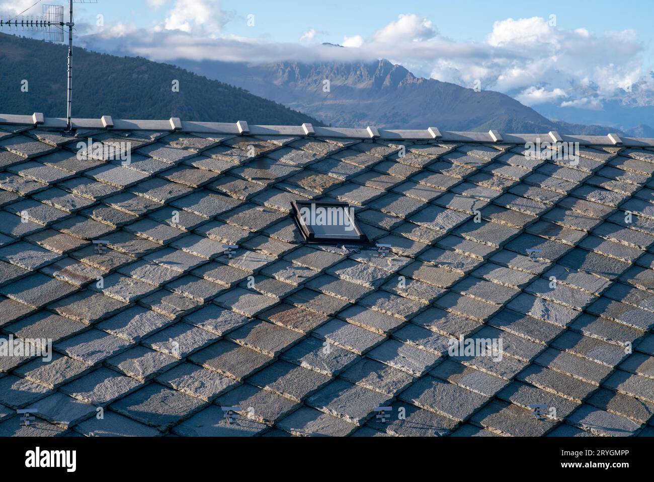 Dach mit Steinkacheln, typisch für Berghäuser, blaue graue Granitsteine, Berge im Hintergrund. Wärmedämmung, Energieklasse. Stockfoto