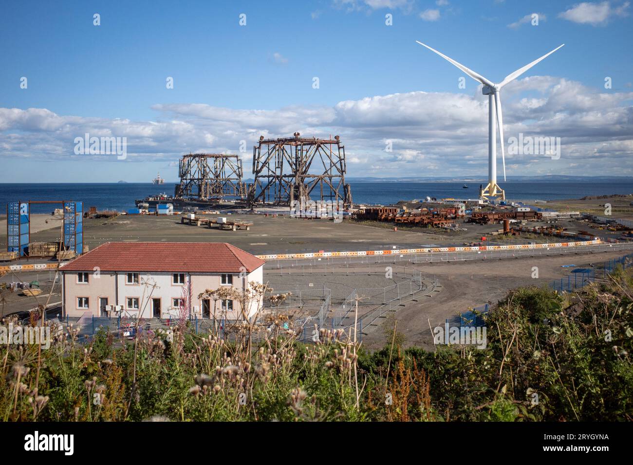 Landschaftsblick auf Firth of Forth in Methil, East Fife, Schottland. Zwei Bohrinseln in einer Werft außer Betrieb genommen, eine Windturbine und blauer Himmel. 2023 Stockfoto