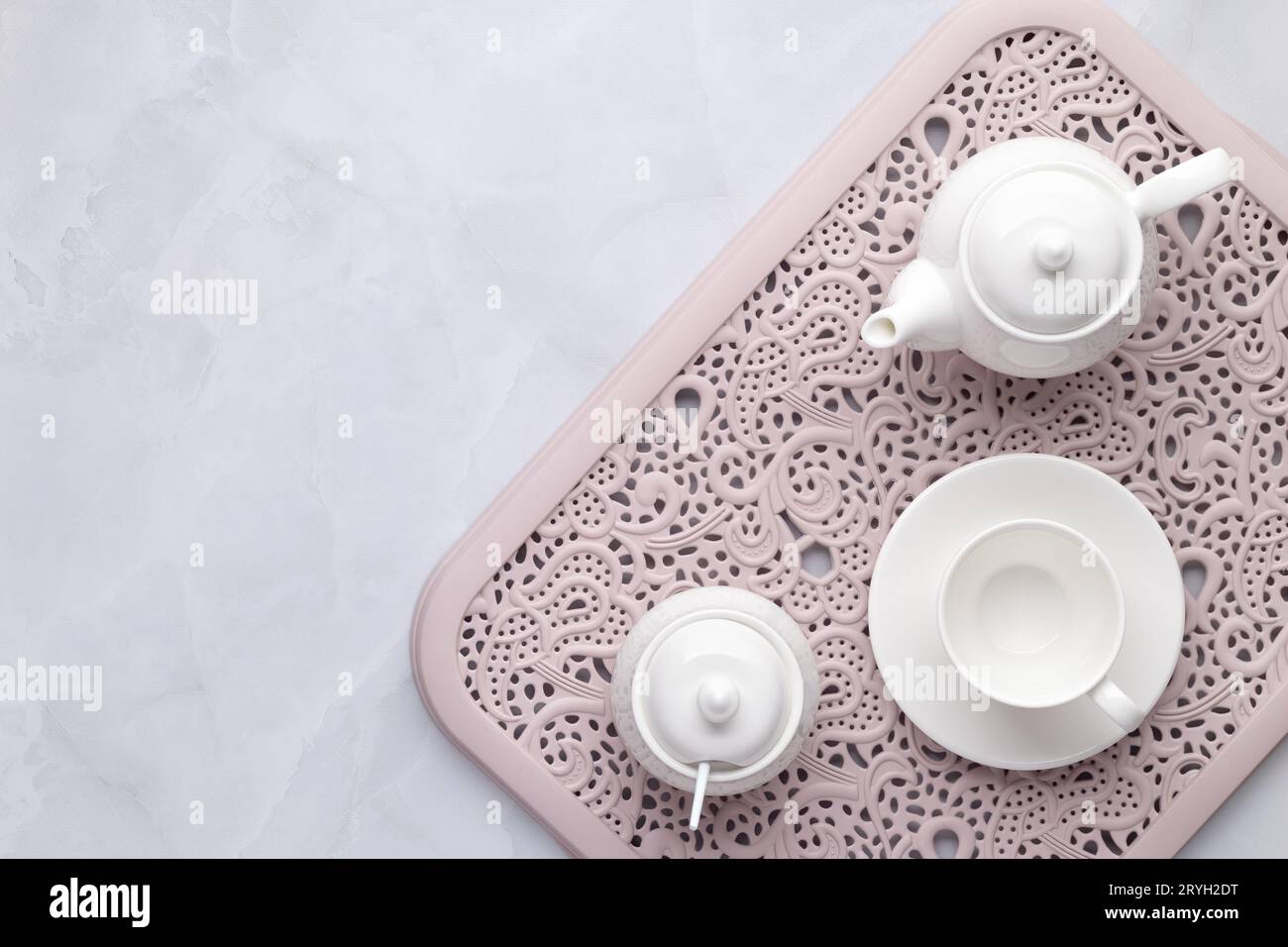 Tee-Party am Morgen. Weiße Teekanne aus Keramik, Tasse und Zuckerschale auf einem rosa durchbrochenen Tablett. Grauer Marmorhintergrund. Tischeinstellung, flach, Draufsicht. Servin Stockfoto