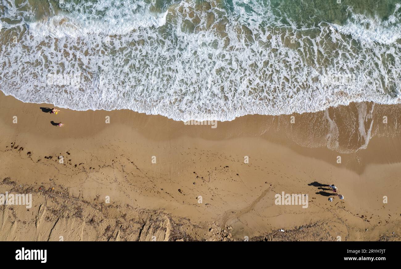 Aus der Vogelperspektive sehen Sie Menschen, die auf Sand am Strand laufen. Stürmische Wellen, idyllischer Strand im Winter. Stockfoto