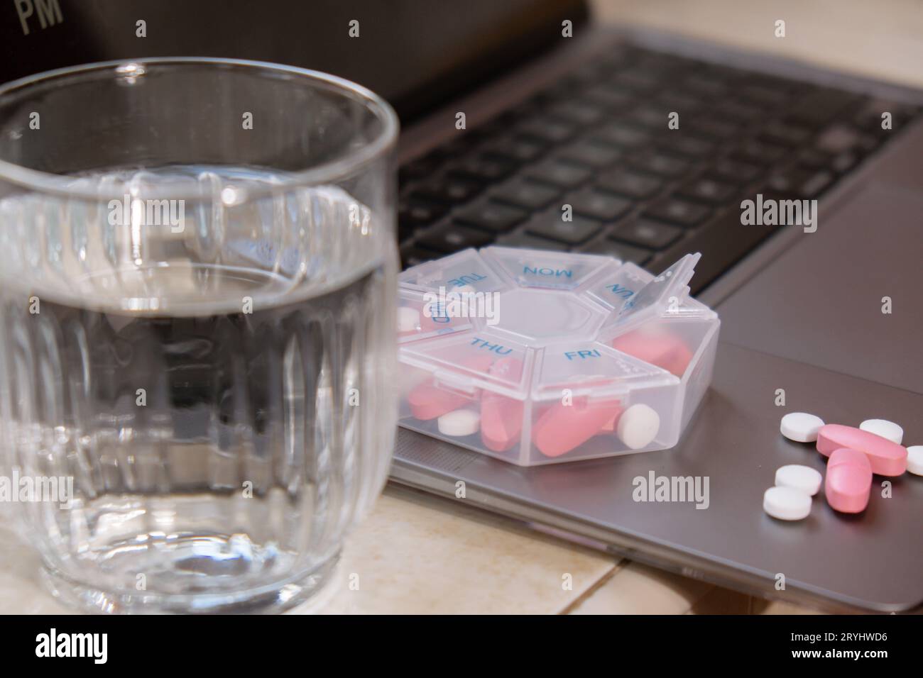 Organisator wöchentliche Shots mit Glas Wasser auf Arbeitsplatz Hintergrund und Laptop Closeup der medizinischen Pille Box mit Dosen von Tabletten Stockfoto