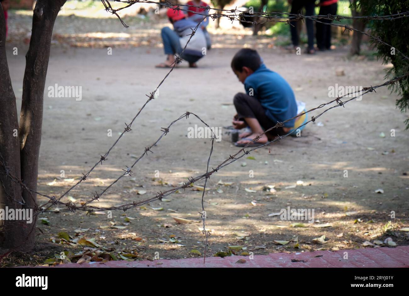 Unbekannte Kinder, die auf einem Spielplatz hinter einem Stachelzaun spielen Stockfoto