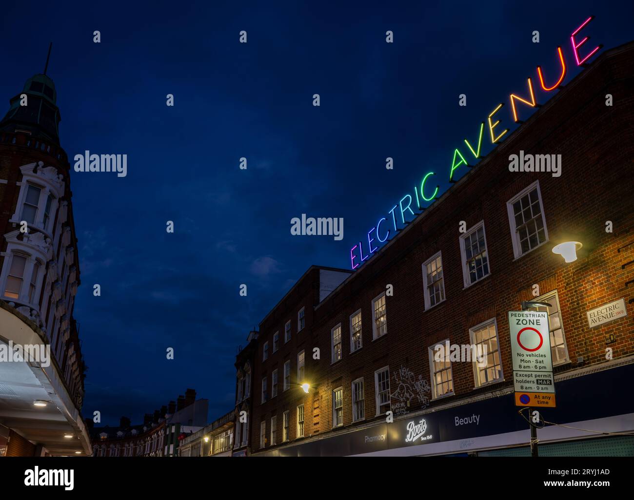 Brixton, London, Großbritannien: Electric Avenue in Brixton bei Nacht. Von der Brixton Road mit dem farbenfrohen Neonschild Electric Avenue aus gesehen. Stockfoto