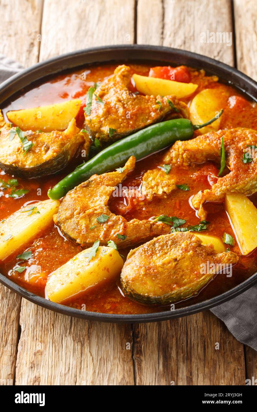 Bengali FischCurry Macher Jhol mit Kartoffeln auf dem Teller auf dem Holztisch. Vertikal Stockfoto