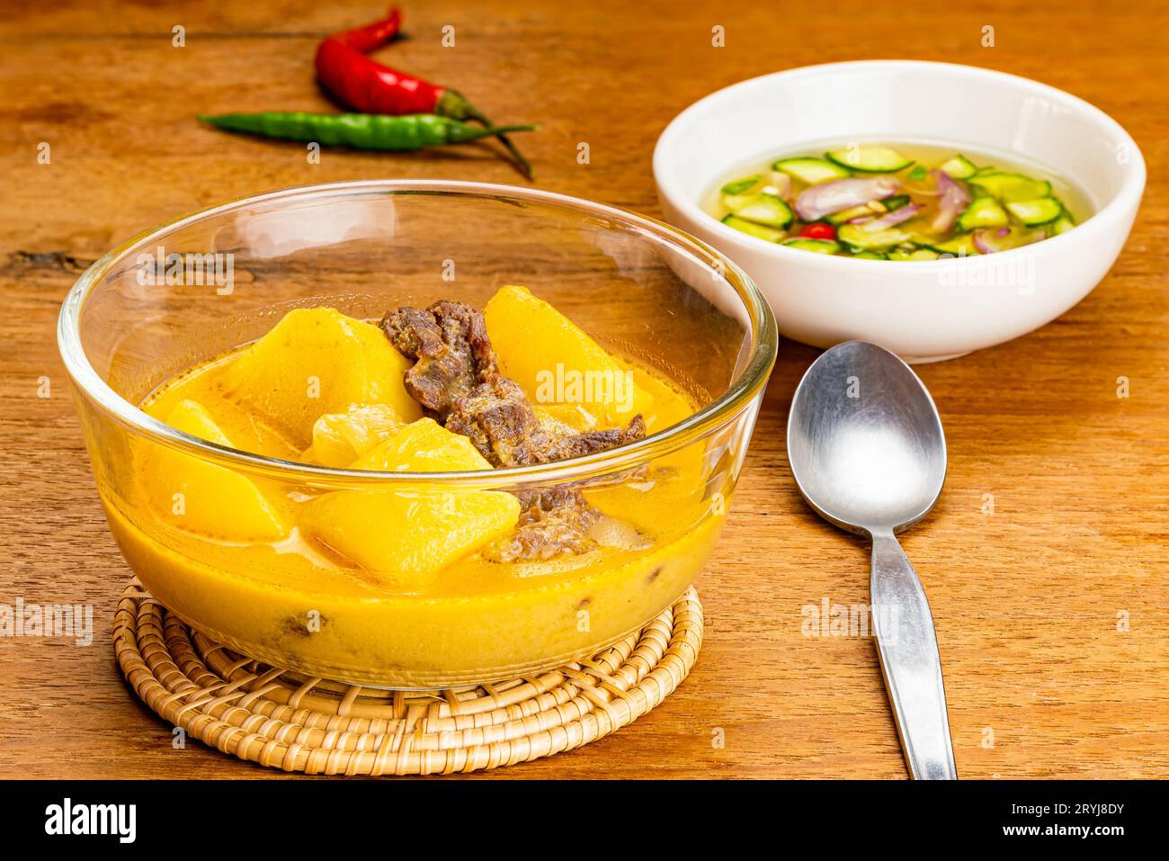Traditionelle köstliche hausgemachte Kartoffeln, Chili, Rinderzwiebeln und Kokosmilchcurry in transparenter Glasschale auf Bambusmatte. Stockfoto