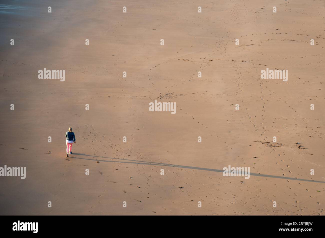 Nicht erkannte Person, die bei Sonnenuntergang am Sandstrand spaziert. Gesunder Lebensstil. Sport im Freien Stockfoto