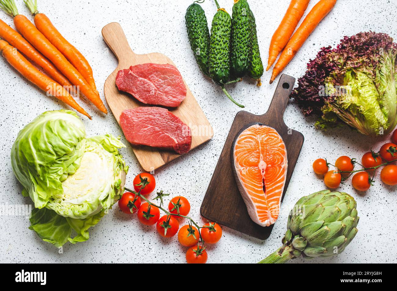 Verschiedene rohe Lebensmittel: Gemüse, Rindfleischsteak, Fisch Lachsfilet auf hölzernen Schneidebrettern, weiße rustikale Tischsicht Stockfoto