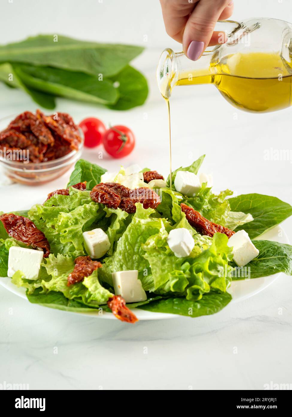 Salat aus sonnengetrockneten Tomaten, Käse und Salatblättern. Olivenöl gießt auf Salat Stockfoto