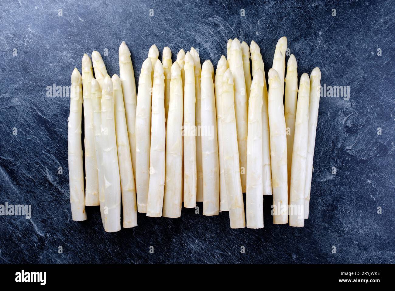 Roher weißer Spargel, der in einer Reihe als Nahaufnahme mit kopiertem Platz oben auf grauem Hintergrund dargestellt wird Stockfoto