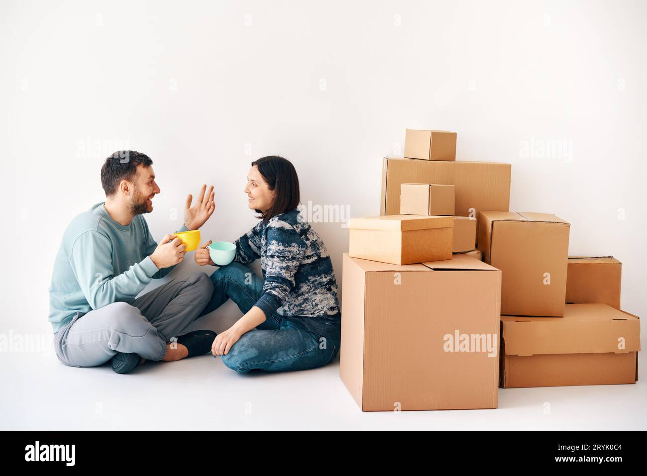 Glückliches, sorgloses Paar, das am Umzugstag auf dem Boden in ihrer neuen Wohnung sitzt. Stockfoto