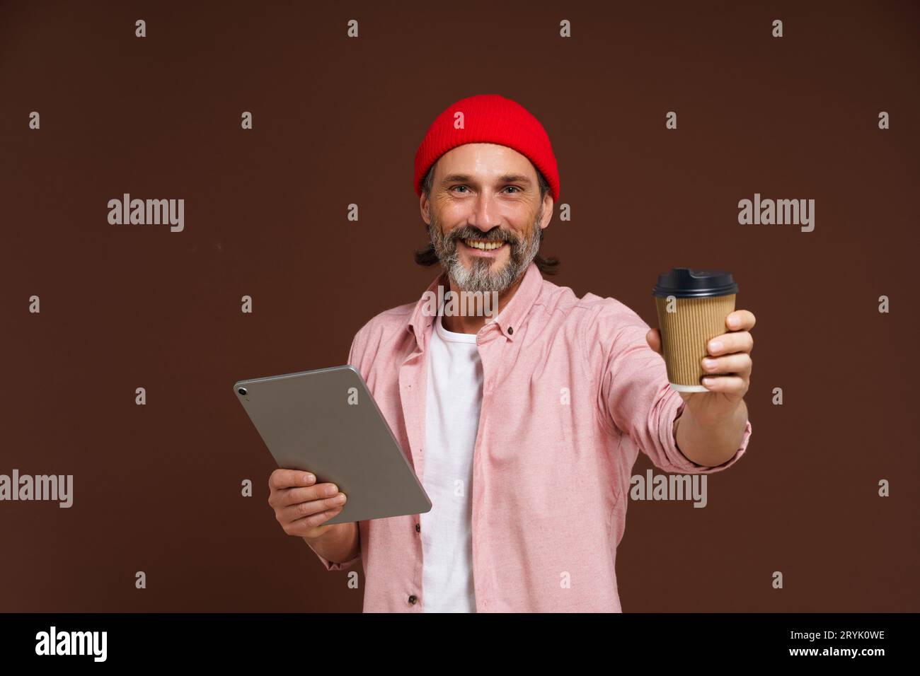 Arbeits- und Kaffeekonzept. Ein lächelnder reifer Mann in legerer Kleidung hält das Tablet in der Hand und bietet eine Tasse mit Kaffee in der Hand Stockfoto