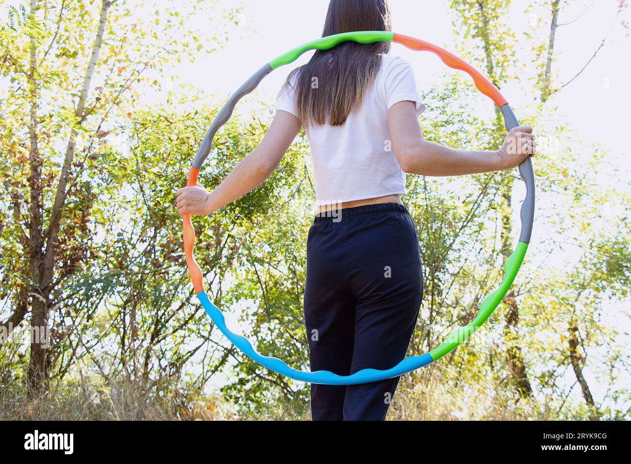 Im Sommer in einem Park in der Ukraine macht eine junge Frau mit einem Sportreifen auf der Taille Fitness mit einem Reifen und hält ihre Figur, Fitness Stockfoto