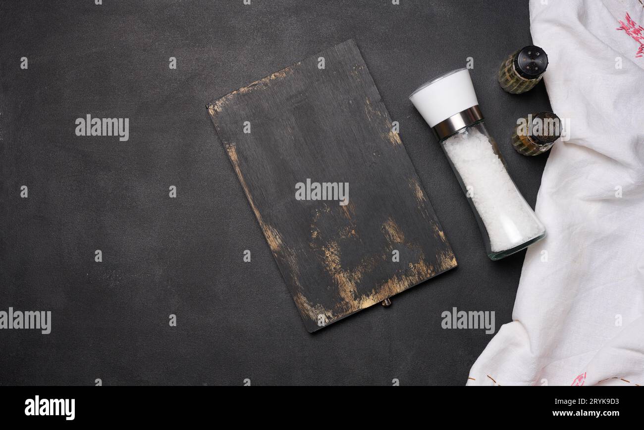 Leeres schwarzes Holzbrett, Salz in einer Glasflasche auf einem schwarzen Tisch, Draufsicht Stockfoto