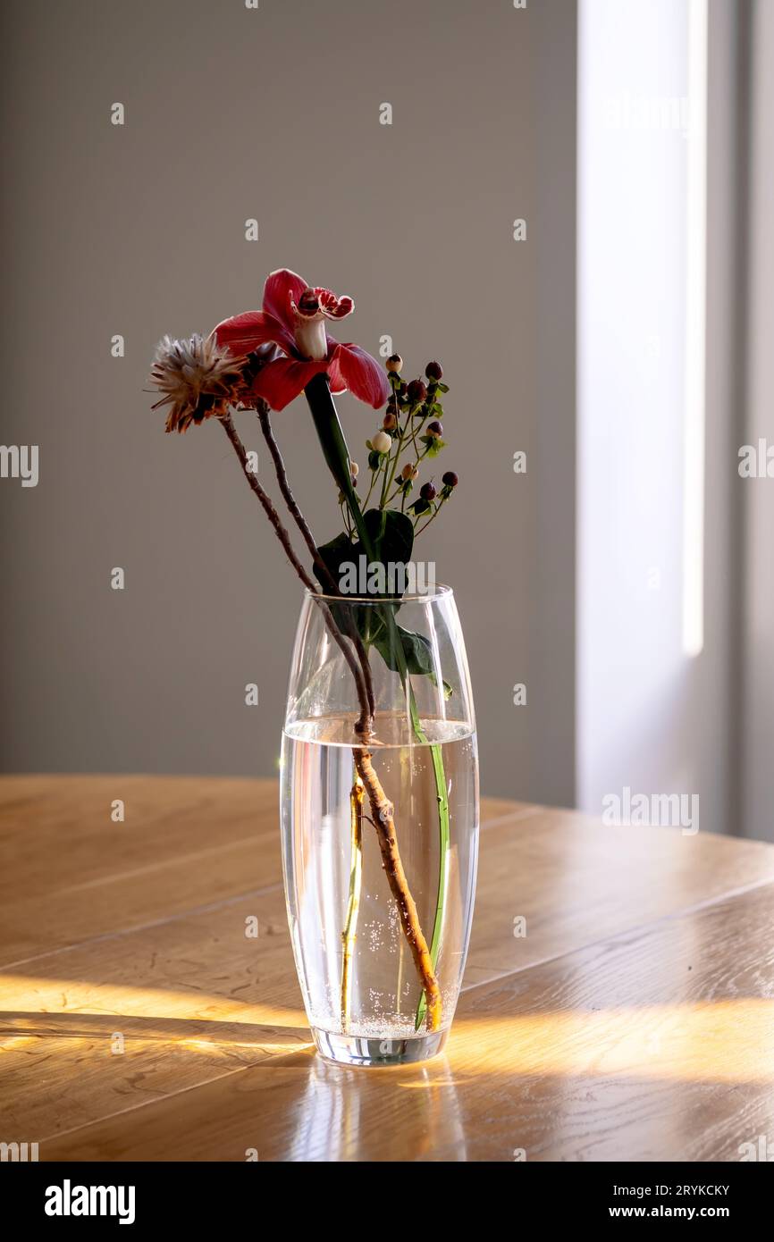 Ein Blumenstrauß in einer transparenten Vase auf einem Holztisch in den Sonnenstrahlen. Stockfoto