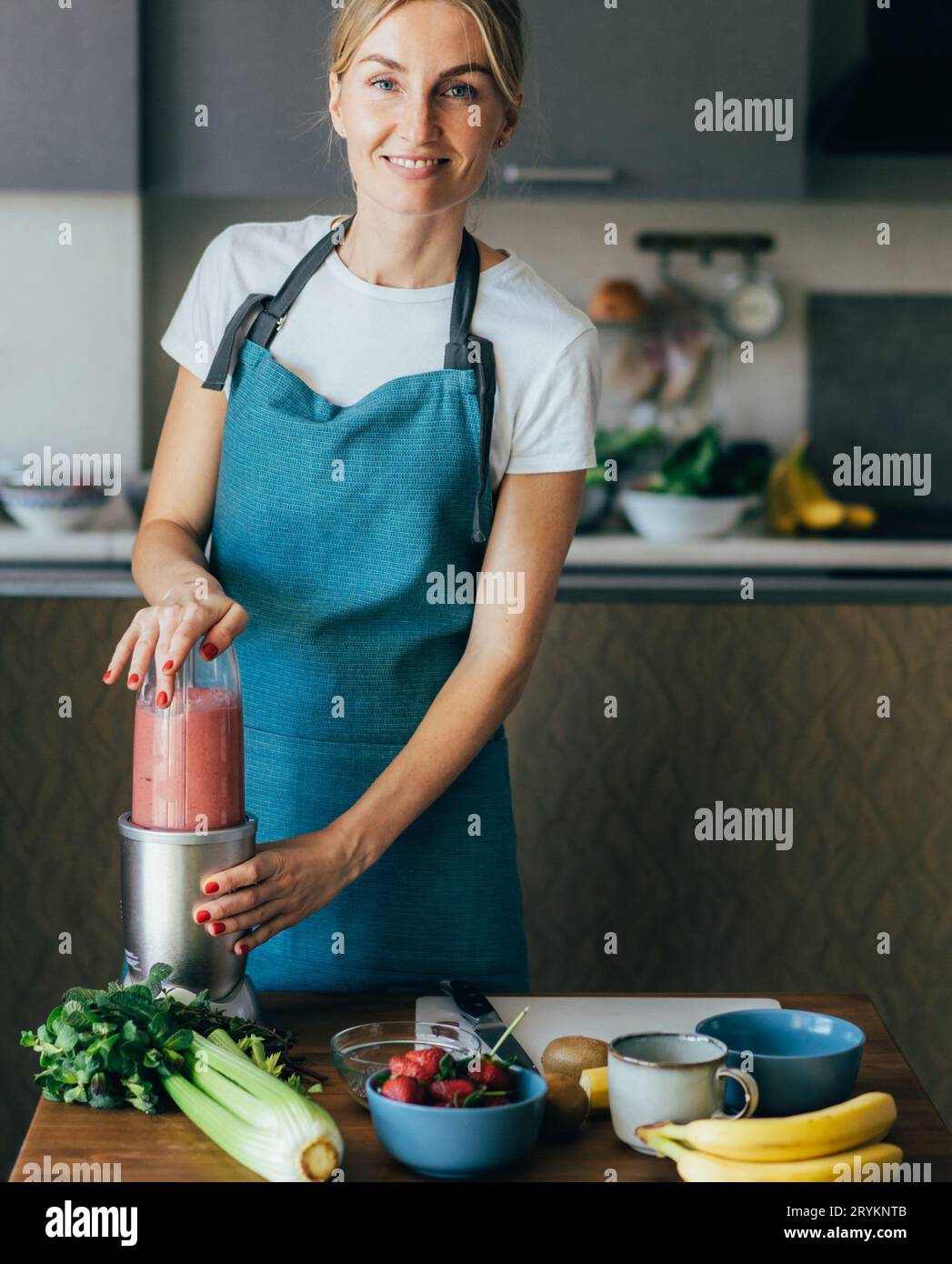 Junge fröhliche glückliche gesunde Frau, die Beeren Smoothie in einem Mixer in der Küche macht. Technologisch moderne Geräte zum Kochen. Stockfoto