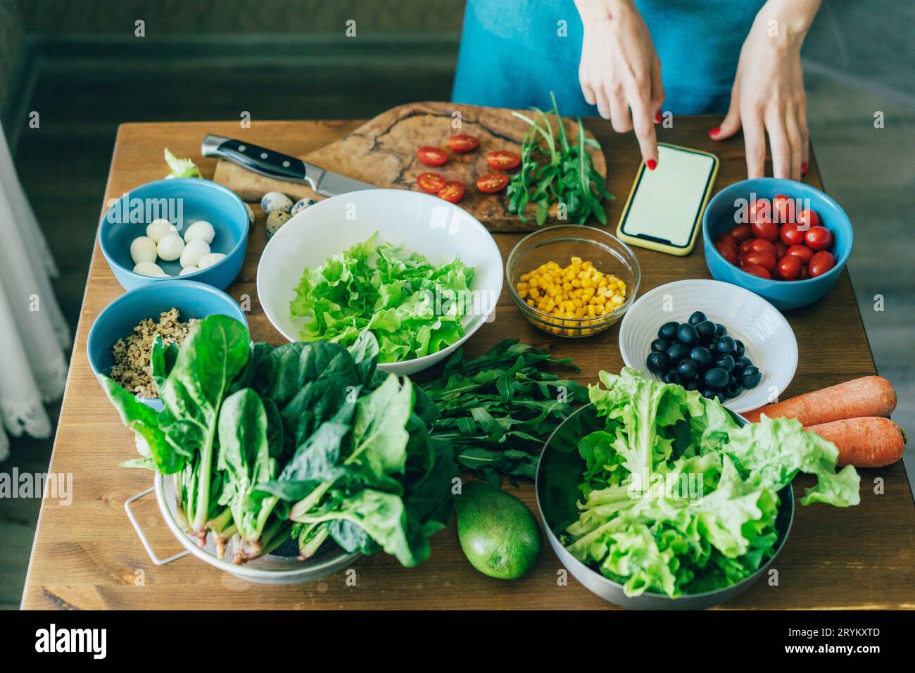 Nahaufnahme eines Küchentisches mit vegetarischen Salatzutaten. Frauenhände im Telefonbuch. Stockfoto