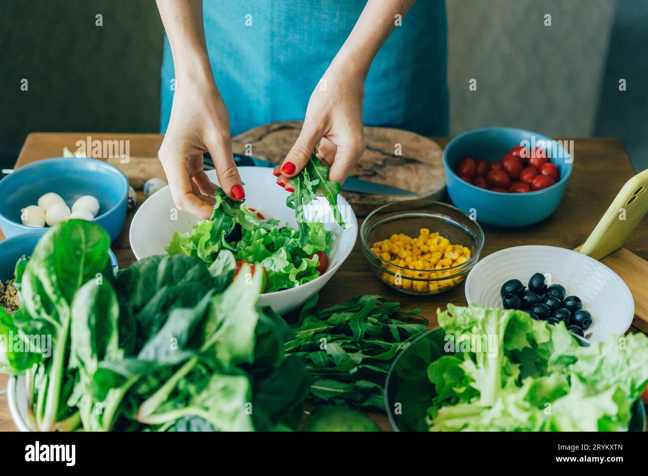 Draufsicht auf den Küchentisch mit Zutaten für die Zubereitung eines Salats der europäischen Küche und den weiblichen Händen der Köchin. Stockfoto