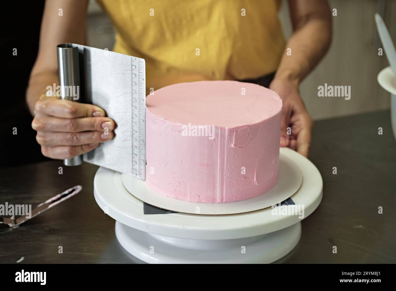 Frau verteilt rosa Sahne auf Kuchen, Nahaufnahme. Kuchenherstellung, selektiver Fokus Stockfoto