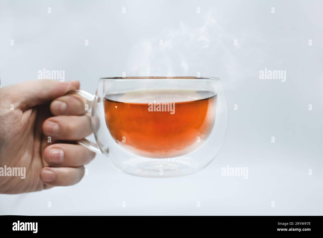 Hand des Mannes hält eine transparente Tasse mit Tee. Isoliert auf weißem Hintergrund. Alpha Stockfoto