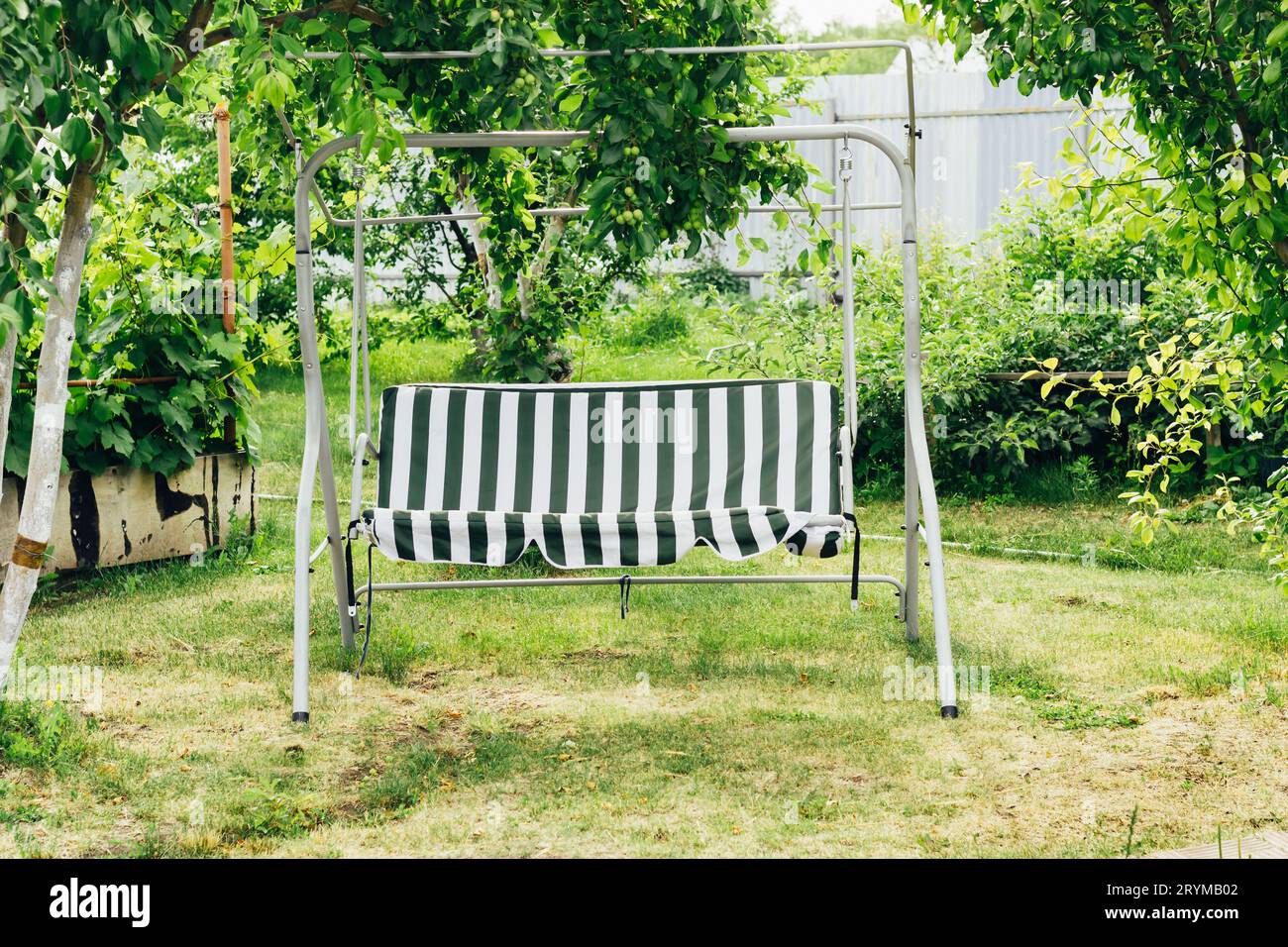 Schwingen Sie zwischen Bäumen im Garten. Cottagecore und Staycation zu Hause. Sommergarten mit Platz für Erholung und Entspannung Stockfoto